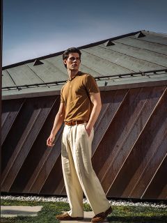 Un homme en polo marron et pantalon beige se promène par une journée ensoleillée devant un bâtiment moderne avec un toit en métal.
