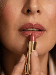 Gros plan d'une femme appliquant du rouge à lèvres violet sur ses lèvres avec un tube de rouge à lèvres doré.