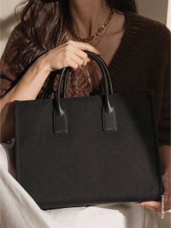 Une femme portant un pull marron tient un grand sac à main noir avec deux anses et a une couverture blanche sur les genoux.