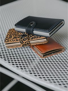 Trois portefeuilles - noir, imprimé léopard et marron - sont posés sur une table en treillis métallique blanche.