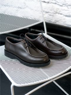 Une paire de chaussures à lacets en cuir marron foncé est posée sur une chaise en treillis métallique blanc.