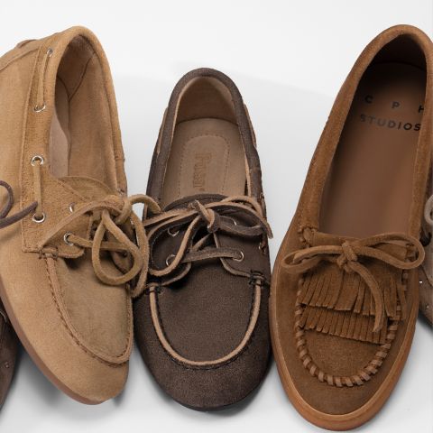 Trois mocassins en daim marron avec lacets sont disposés côte à côte, chacun présentant des coutures et des détails différents sur un fond blanc.