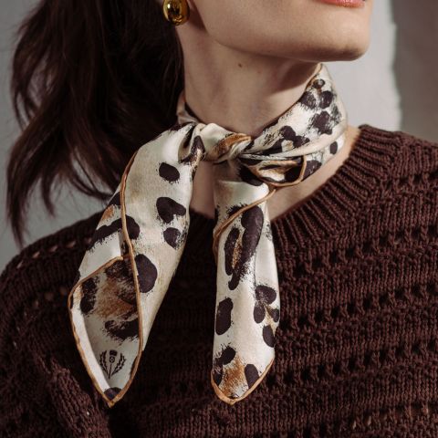 Une femme porte un pull en tricot marron et une écharpe crème à imprimé léopard nouée autour du cou.
