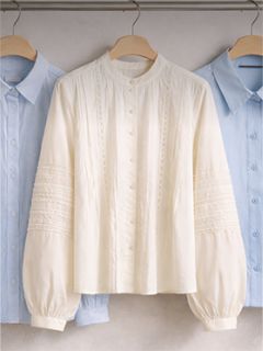 Trois chemises boutonnées avec col sur cintres, une chemise blanche texturée au milieu et deux chemises bleu clair de chaque côté.