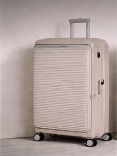 Valise rigide beige à rainures horizontales, posée verticalement sur quatre roues, avec poignée télescopique déployée.