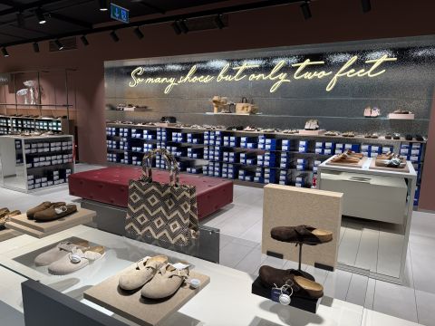 Intérieur d'un magasin de chaussures avec des sandales exposées, un sac fourre-tout à motifs et un néon indiquant "Tant de chaussures, mais seulement deux pieds".