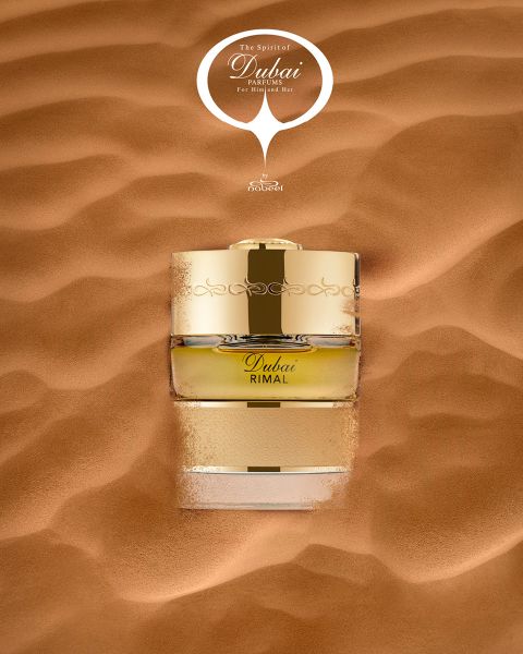 Un flacon de parfum doré avec l'inscription « Dubai Rimal » est partiellement enfoncé dans le sable lisse du désert, au-dessus se trouve l'inscription « The Spirit of Dubai ».
