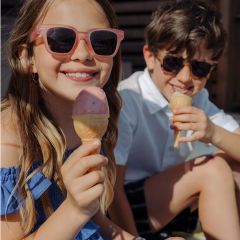 Deux enfants souriants avec des lunettes de soleil savourent des cornets de glace en plein air par une journée ensoleillée.
