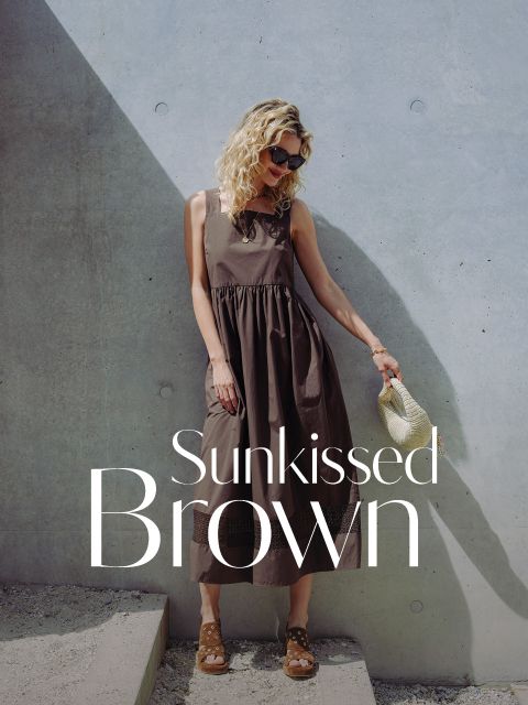 Une femme vêtue d'une robe marron sans manches se tient devant un mur en béton, tenant un sac en paille. Le texte dit "Sunkissed Brown".