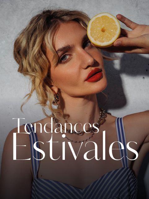 Une femme dans un haut rayé tient une demi-citron devant son œil. Elle a des cheveux blonds ondulés et du rouge à lèvres rouge. Le texte dit : « Tendances Estivales. ».