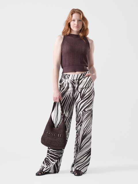 Une femme porte un haut marron sans manches, un pantalon large à motif zèbre, des sandales noires et un sac Coach marron.