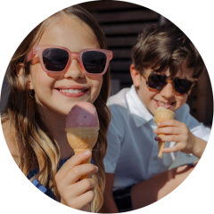Deux enfants souriants avec des lunettes de soleil savourent des cornets de glace en plein air par une journée ensoleillée.