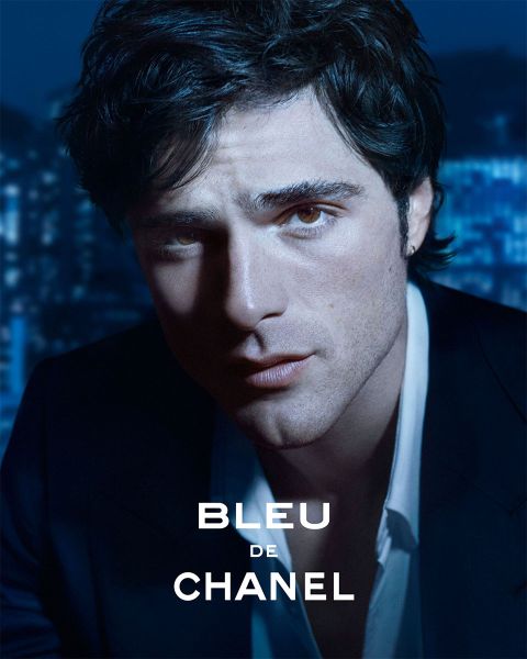 Un homme en costume sombre regarde attentivement la caméra, tandis que les lumières de la ville s'estompent en arrière-plan ; le texte dit "Bleu de Chanel".