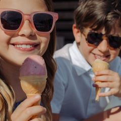 Deux enfants souriants avec des lunettes de soleil savourent des cornets de glace en plein air par une journée ensoleillée.