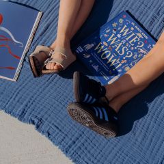 Deux personnes sont assises les jambes tendues sur une couverture bleue en plein air, avec des sandales et des baskets, à côté de deux livres ouverts, dont l'un a une couverture bleue.