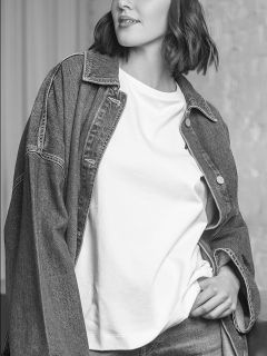 Une femme en veste en jean et t-shirt blanc, posant avec une main dans la poche ; l'image est en noir et blanc.