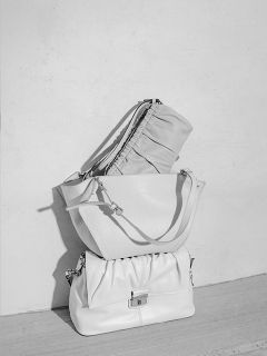 Trois sacs à main élégants aux tons clairs sont posés sur une surface en bois devant un mur simple et clair, et sont soigneusement disposés dans une ambiance minimaliste.