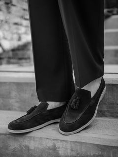Photo en noir et blanc d'une personne portant des mocassins sombres à pampilles et un pantalon de costume, et se tenant sur un escalier en béton extérieur.