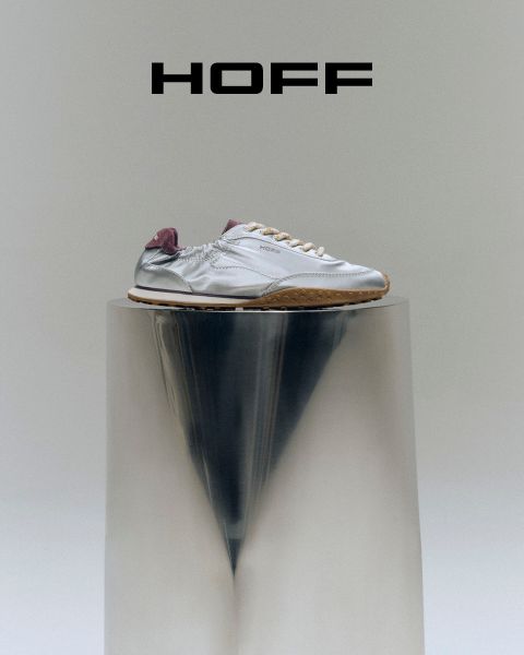 Une basket argentée à talon violet repose sur un socle réfléchissant sous le logo « HOFF » sur un fond gris clair.