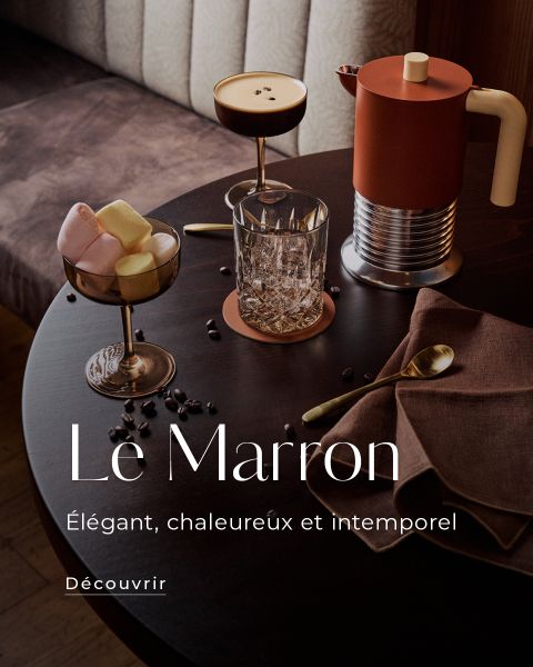 Une table ronde sombre avec des boissons, des marshmallows aux couleurs pastel, une cafetière marron et des couverts dorés. Le texte dit : « Le Marron. Élégant, chaleureux et intemporel. »