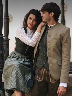 Une femme et un homme en costume traditionnel bavarois sont assis ensemble en plein air, souriant et se regardant.