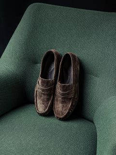 Une paire de mocassins en daim marron repose soigneusement sur un fauteuil rembourré vert.
