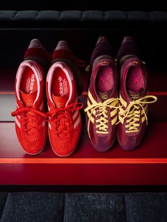 Deux paires de baskets adidas : l'une rouge à rayures blanches, l'autre violette à rayures jaunes, côte à côte sur une surface à rayures rouges.
