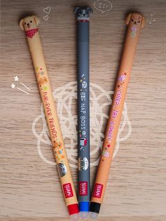 Trois stylos gel mignons avec des motifs d'animaux et des visages sur les capuchons sont alignés sur un support en bois.