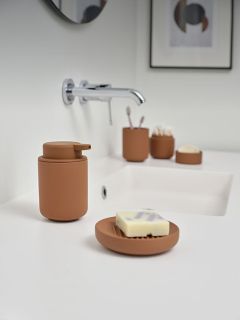 Un lavabo moderne avec distributeur de savon marron, porte-savon et accessoires sur un plan de travail blanc, et un robinet mural monté au-dessus.