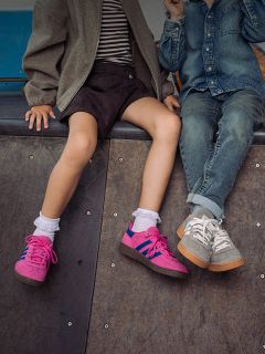 Deux enfants sont assis côte à côte sur une rampe ; on ne voit que leurs jambes et leurs baskets - l'un porte des chaussures roses, l'autre des baskets grises et un jean.