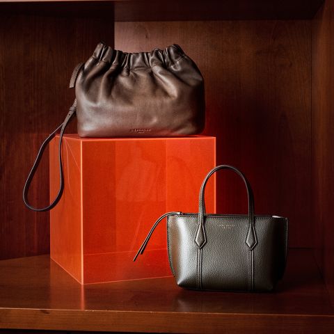 Deux élégants sacs à main en cuir, l'un marron foncé et l'autre vert olive, présentés sur une étagère en bois avec un cube translucide orange.