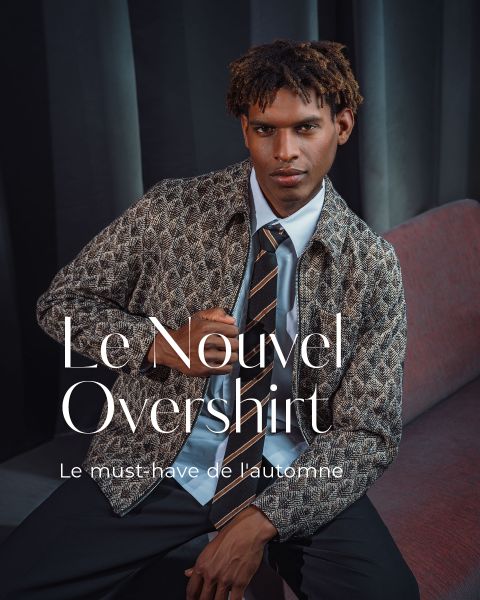 Un homme en surchemise à motifs, cravate et chemise blanche est assis sur un banc rouge. Le texte français est : « Le Nouvel Overshirt. L'incontournable de l'automne. »