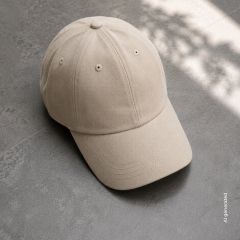 Sur un sol carrelé gris repose une casquette de baseball beige, avec la lumière du soleil et des ombres douces visibles en arrière-plan.