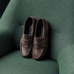Des mocassins en daim marron, posés sur un fauteuil vert texturé.