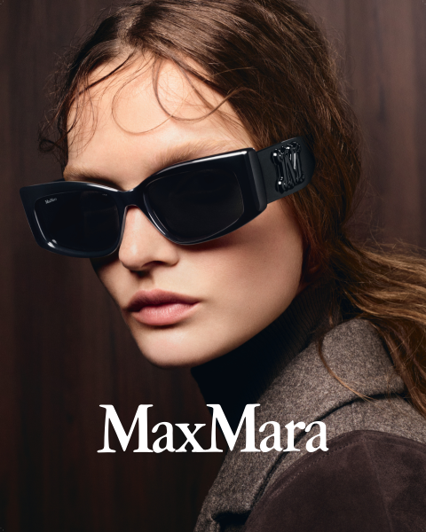 Une femme avec de grandes lunettes de soleil noires et un manteau marron devant un fond en bois foncé, le logo "MaxMara" est visible en bas.