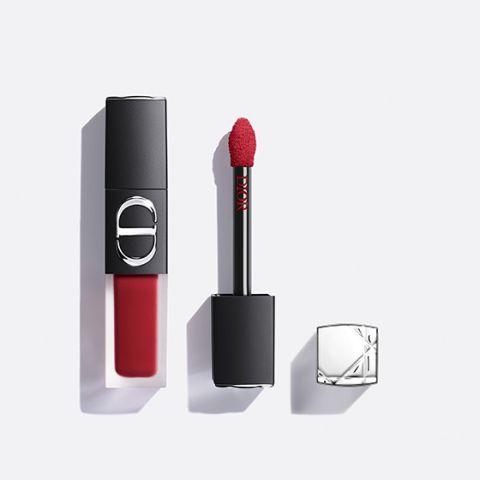 Un rouge à lèvres liquide rouge de Dior, avec son applicateur sorti et son capuchon argenté posé à côté, le tout sur un fond blanc.