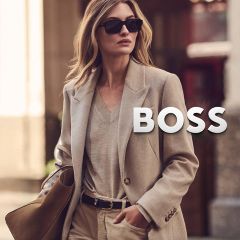 Une femme en blazer beige et lunettes de soleil, portant un sac à main orné du logo BOSS.