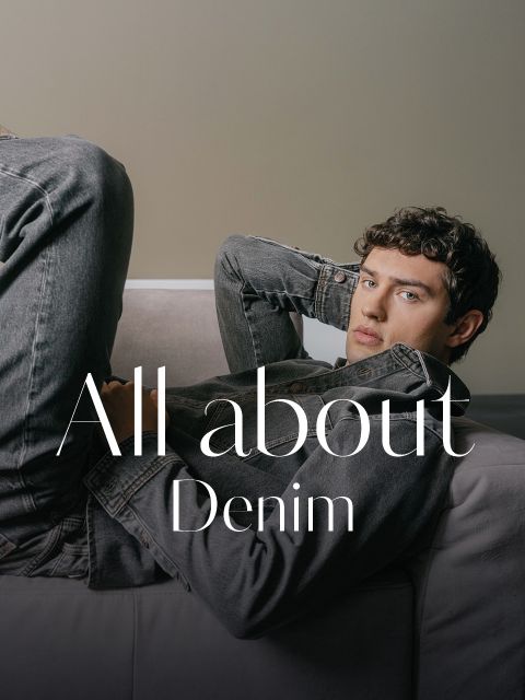 Un jeune homme en veste et jean en denim gris est appuyé sur un canapé, avec le texte "All about Denim" superposé sur l'image.
