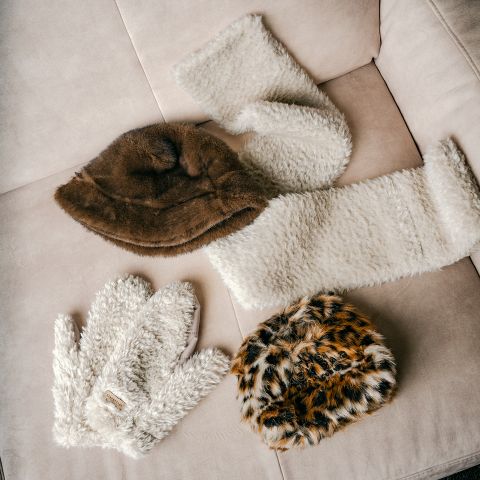 Sur un canapé beige sont posés quatre accessoires d'hiver en fourrure, dont deux bonnets, une écharpe et des gants.