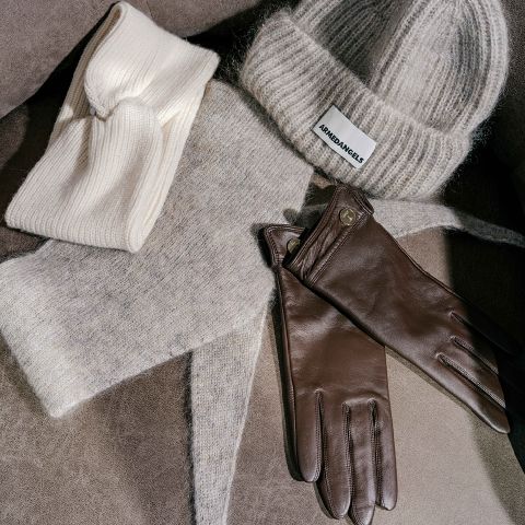 Un bandeau tricoté couleur crème, un bonnet tricoté gris Armedangels, une écharpe grise assortie et une paire de gants en cuir marron.