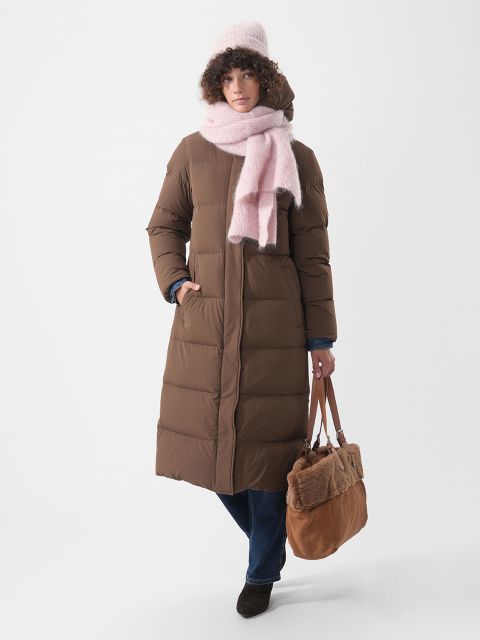 Une personne porte un long manteau matelassé marron, un bonnet rose et une écharpe rose, et elle tient un cabas marron.