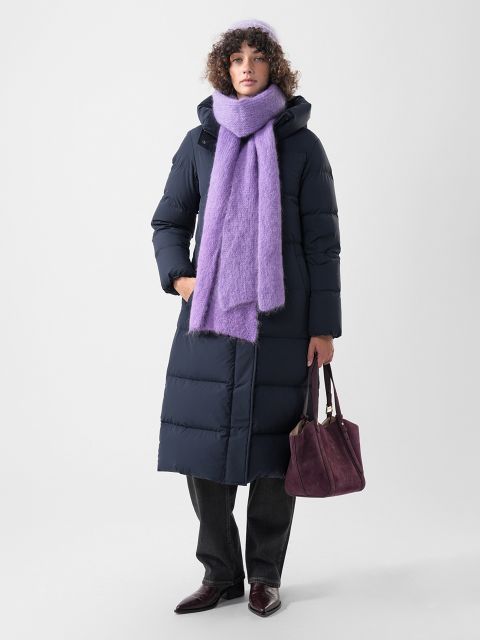 Une personne portant un long manteau doudoune bleu marine, un bonnet violet et une écharpe violette assortie, tenant un sac à main bordeaux.